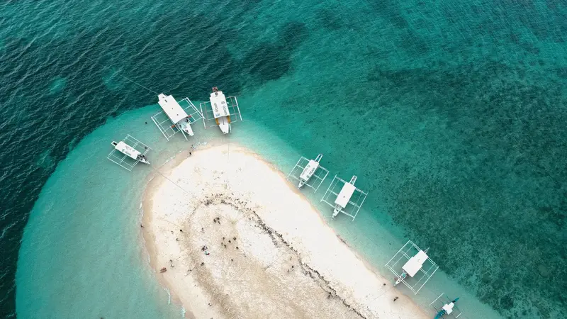 Outrigger boats moored around a white sandbar in clear green water at Kintarkan Island, Bantayan