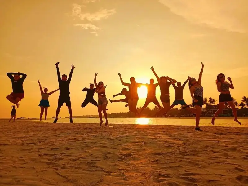 A group of guests leaping on the sand in front of a golden sunset