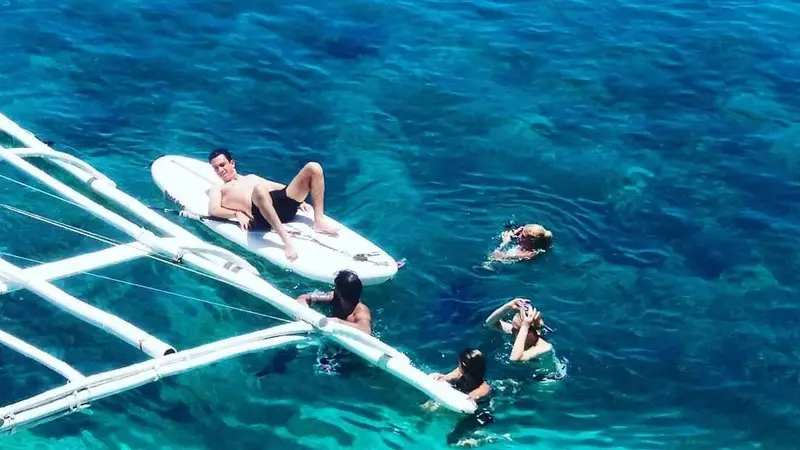 Guests swimming in clear blue water beside the bangka's outrigger off Lamanoc Island