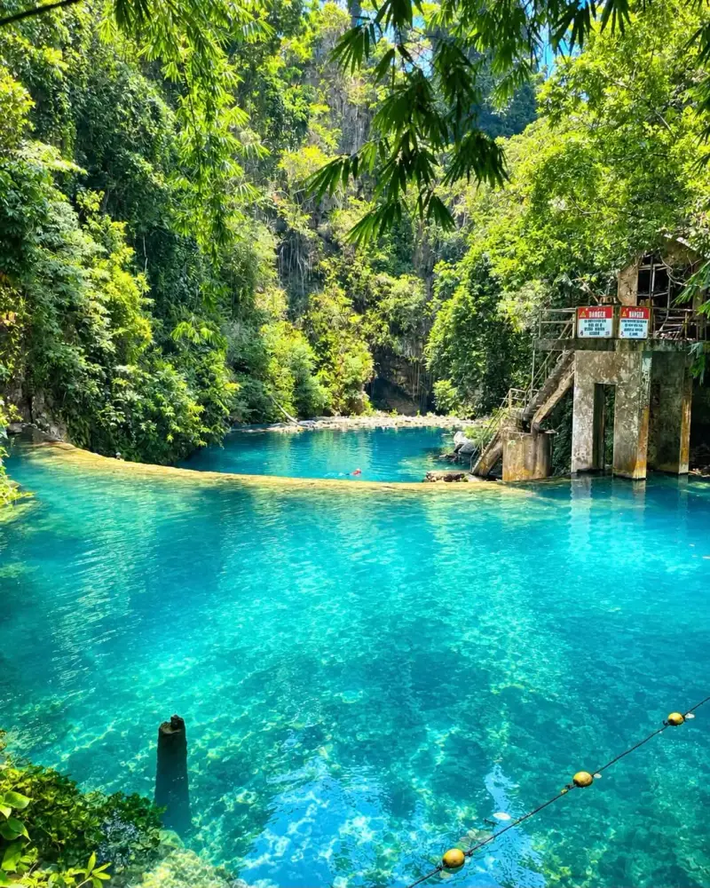 A turquoise pool below a curved rock weir, ringed by jungle, at Kawasan Falls in Badian