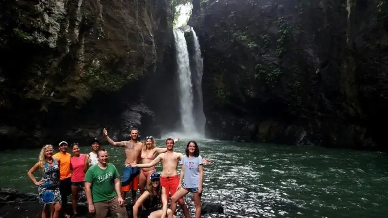 A group of guests standing in the pool below a tall waterfall on Biliran Island