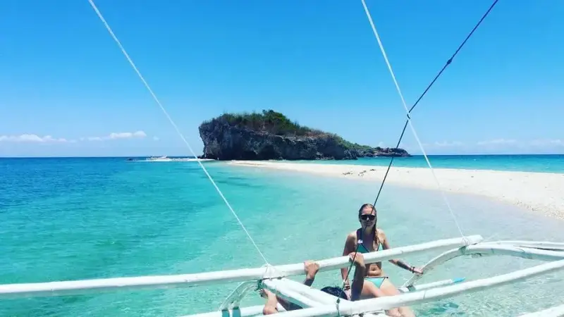 A guest on the outrigger of the bangka as it nears Lamanoc Island's rocky islet and white sandbar