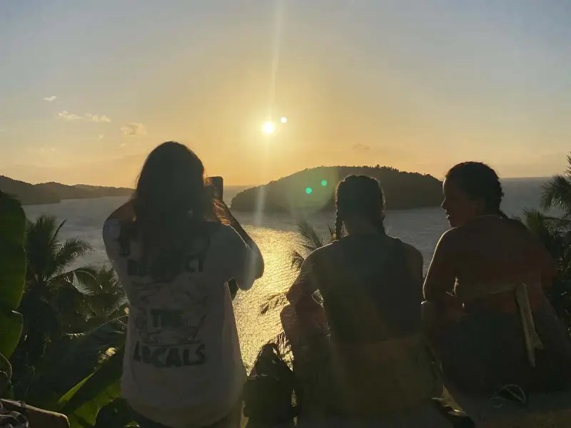 Three guests silhouetted against the setting sun, looking out over the sea and a small island