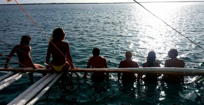 Guests sitting along a bamboo outrigger at dusk, looking out over the sea off Bantayan, Cebu