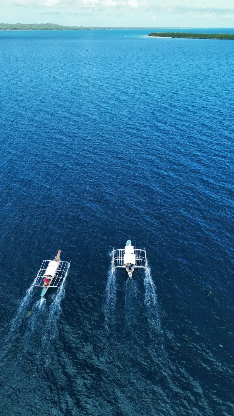 Two outrigger boats crossing deep blue water towards Malapascua Island