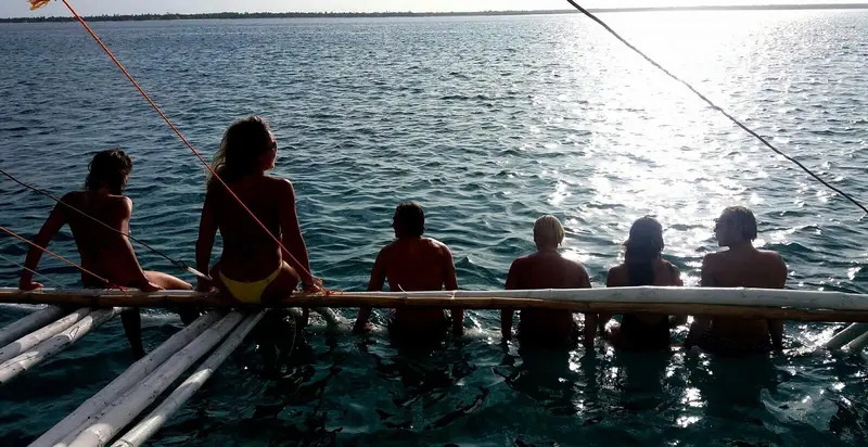 Group sitting along a bamboo outrigger over calm water at dusk