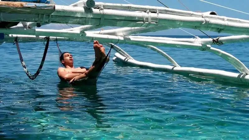 A guest lounging in a hammock slung under the bangka's outrigger, just above the water