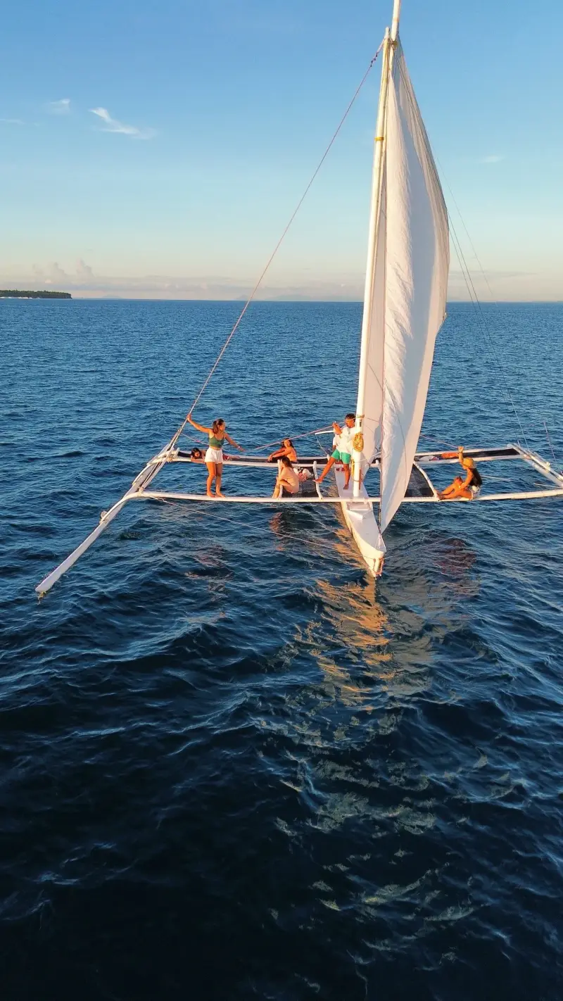 Drone view of a paraw with guests on its outriggers, sailing on open blue water