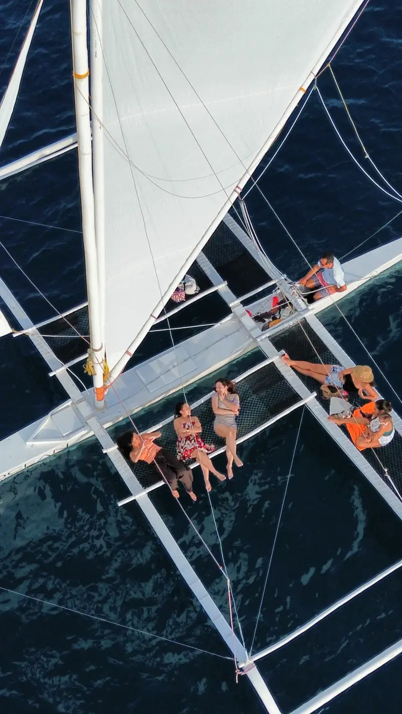 Drone view looking straight down on guests lounging on the paraw's netting beside its white sail, off Santa Fe, Bantayan