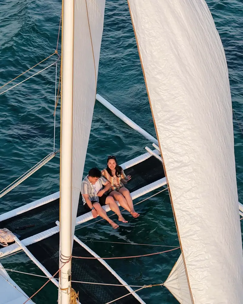 Two guests sitting on the paraw's netting between its two white sails