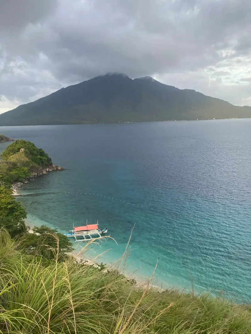 Clear blue cove below green hills with an outrigger boat moored at Sambawan Island, Biliran
